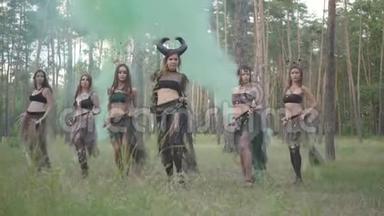 一群身着化妆和神秘服装的女舞者在彩烟中翩翩起舞。 森林仙女，干柴